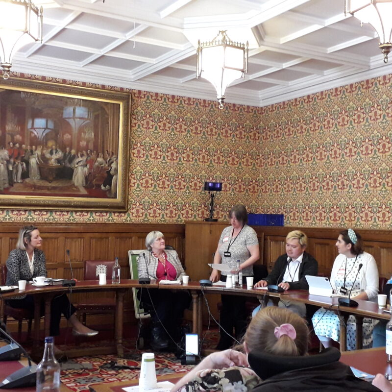 Patsy is standing in the House of Lords talking about her life in a room full of people.